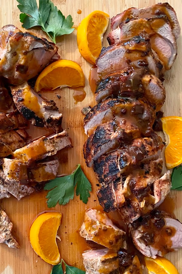 Slice of grilled pork tenderloin with orange wedges.
