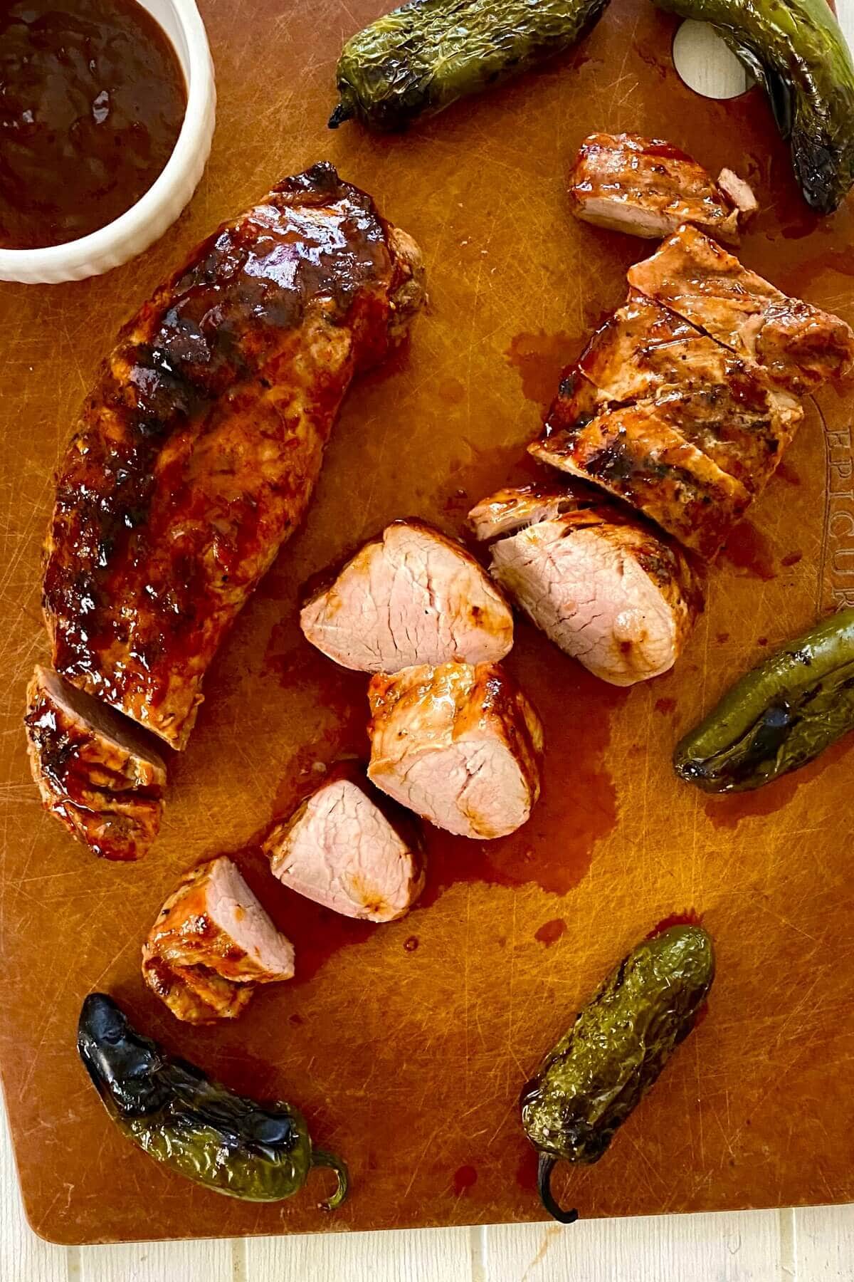 sliced glazed pork tenderloin on a cutting board.