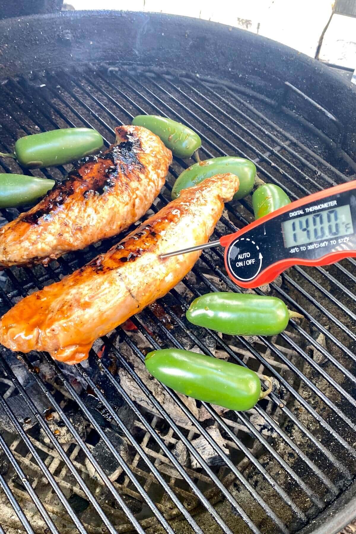 pork tenderloin on a grill with a digital thermometer at 140 degrees F.