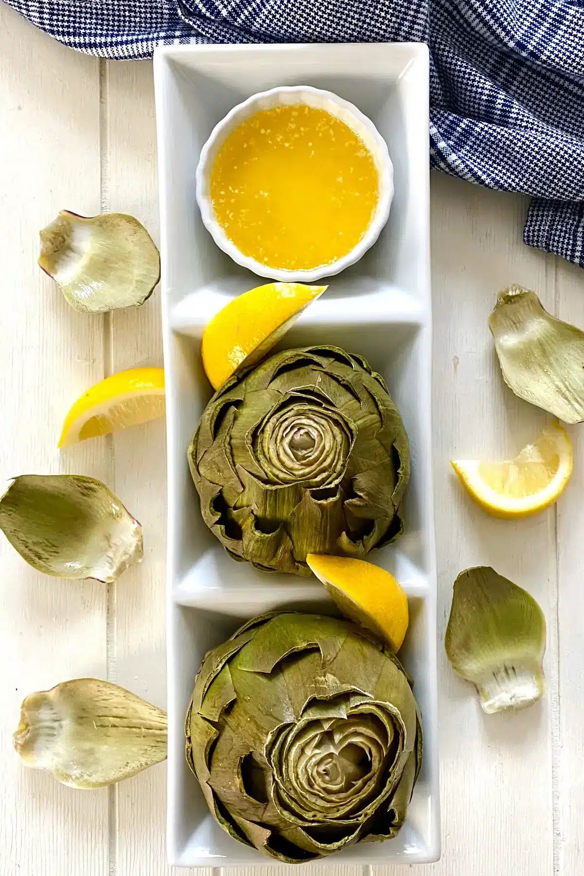 2 cooked microwave artichokes with melted butter and lemon wedges.