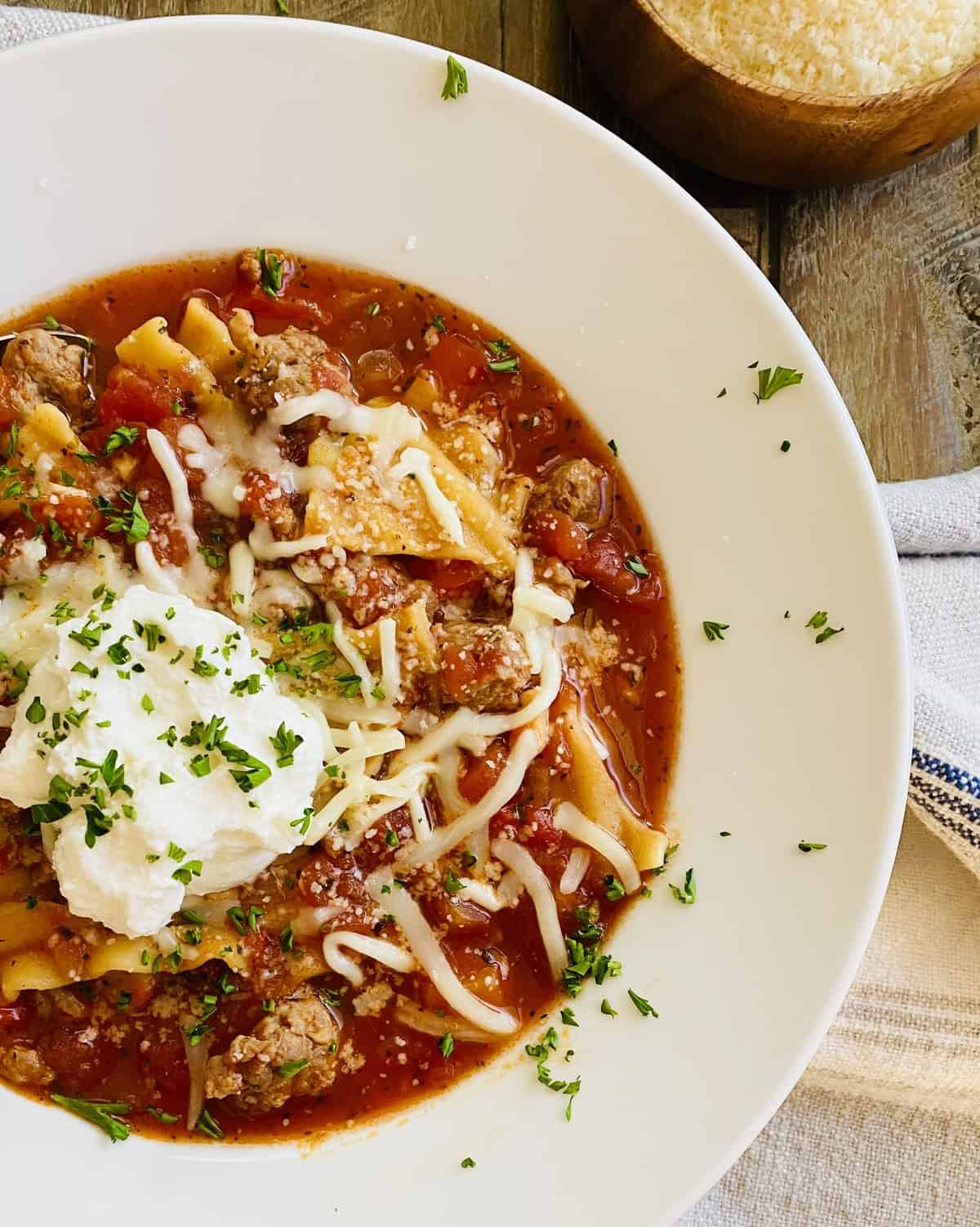 A white bowl of lasagna soup topped with ricotta cheese.