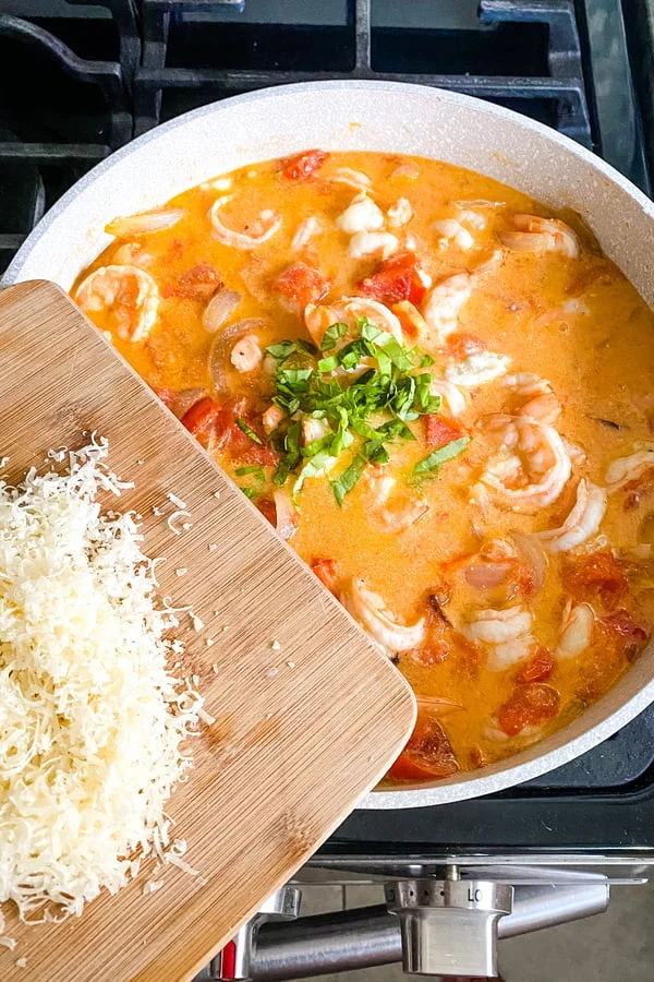 adding fresh basil and Parmesan cheese to shrimp with tomato sauce dish