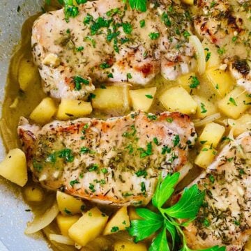 2 pork chops with apples and onions in a pan.