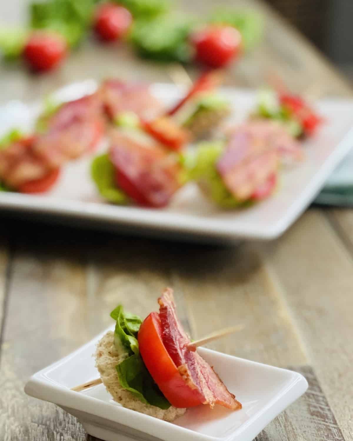 A single toothpick with bacon, lettuce and tomato and a plate.