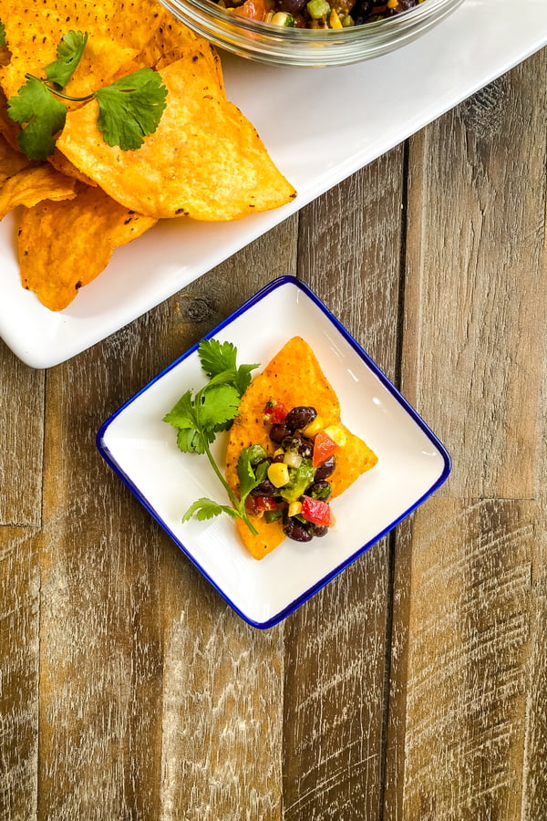 A Dorito chip with Texas caviar bean dip on a small plate.