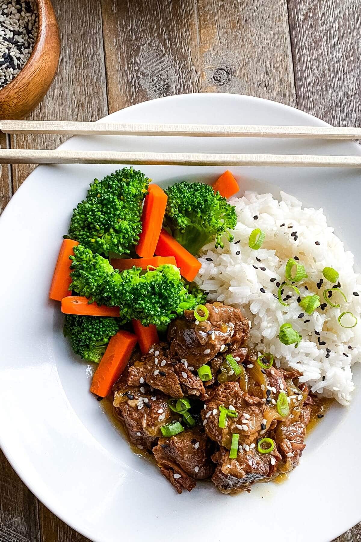A bowl of Asian beef stew with rice, broccoli and carrots.
