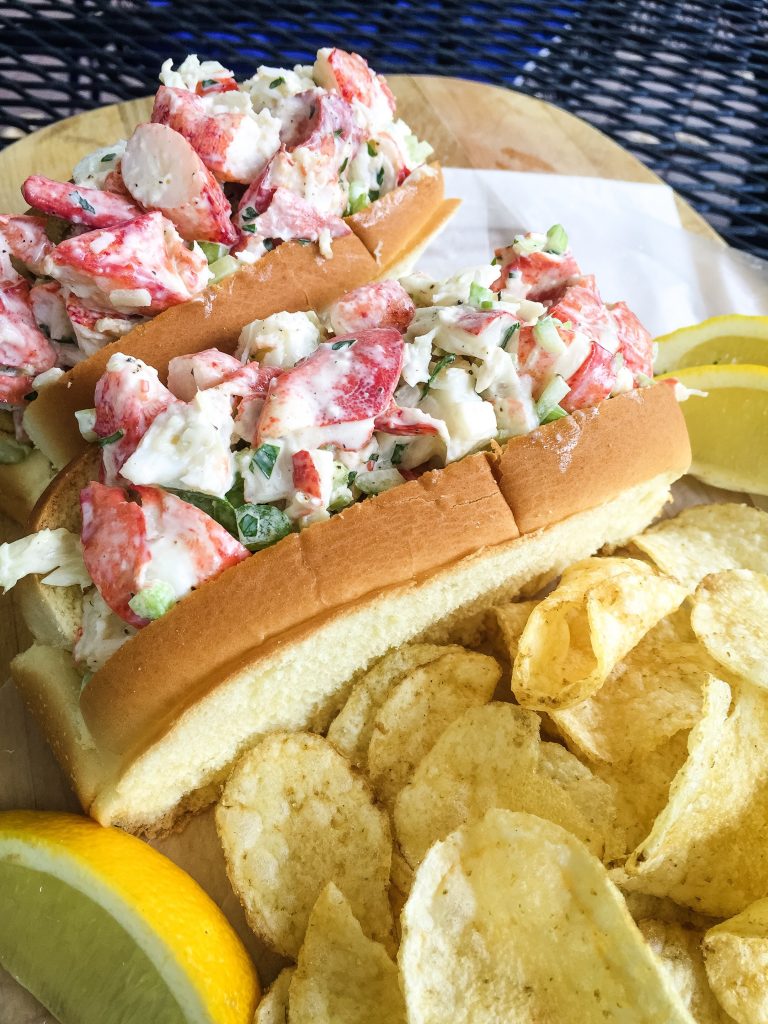 2 cold lobster rolls with potato chips and lemon wedges.
