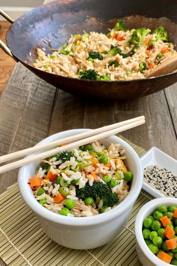 bowl of fried rice with chicken with chopsticks and a wok full of fried rice