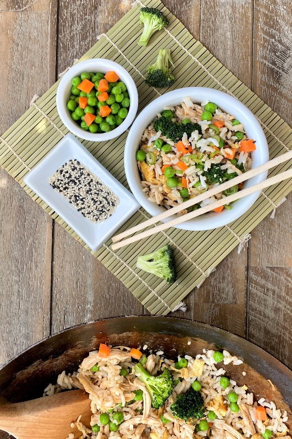 overhead photo of a bowl of Asian chicken and rice with chopsticks and sesame seeds