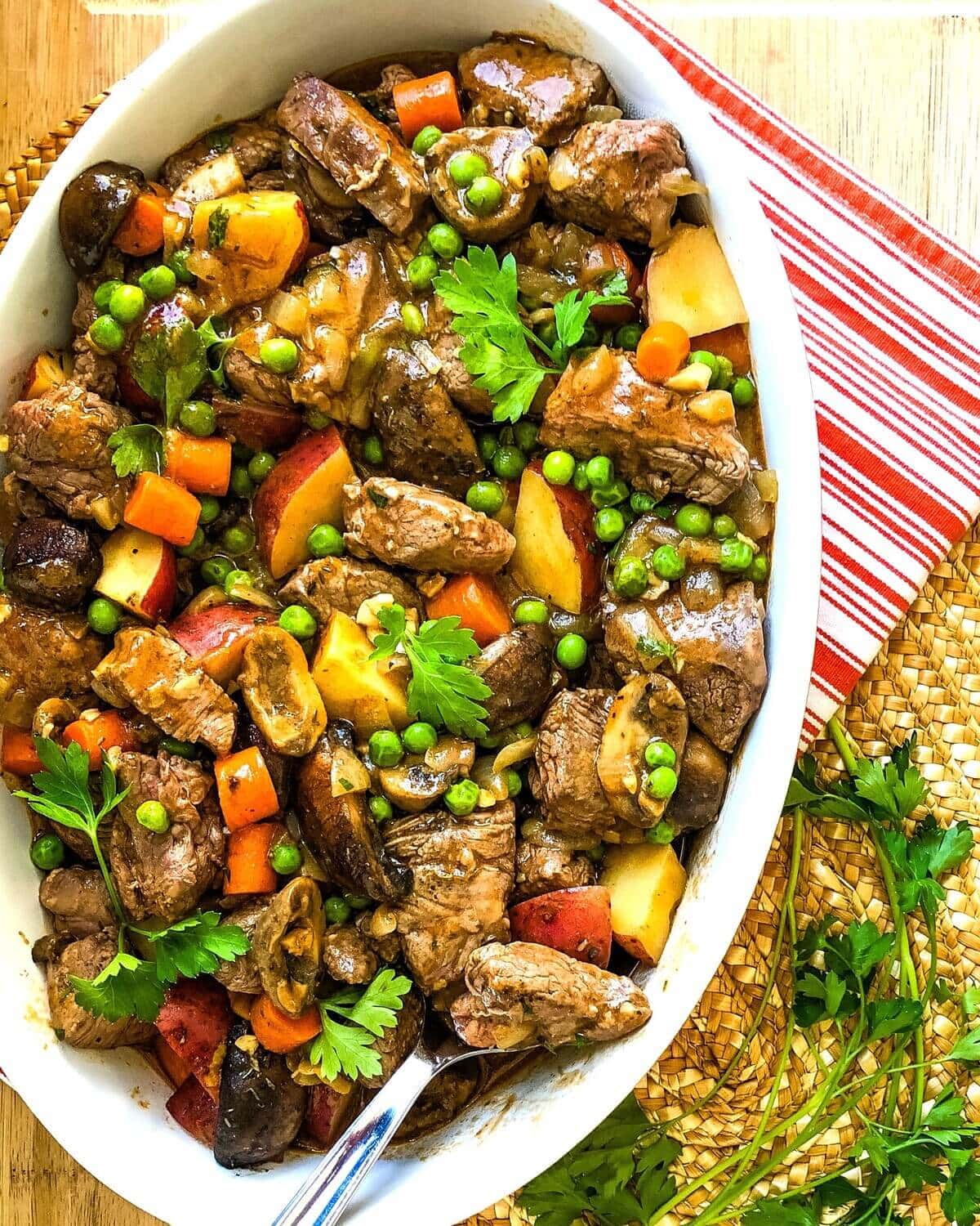 serving dish with beef, potatoes, carrots and mushrooms.