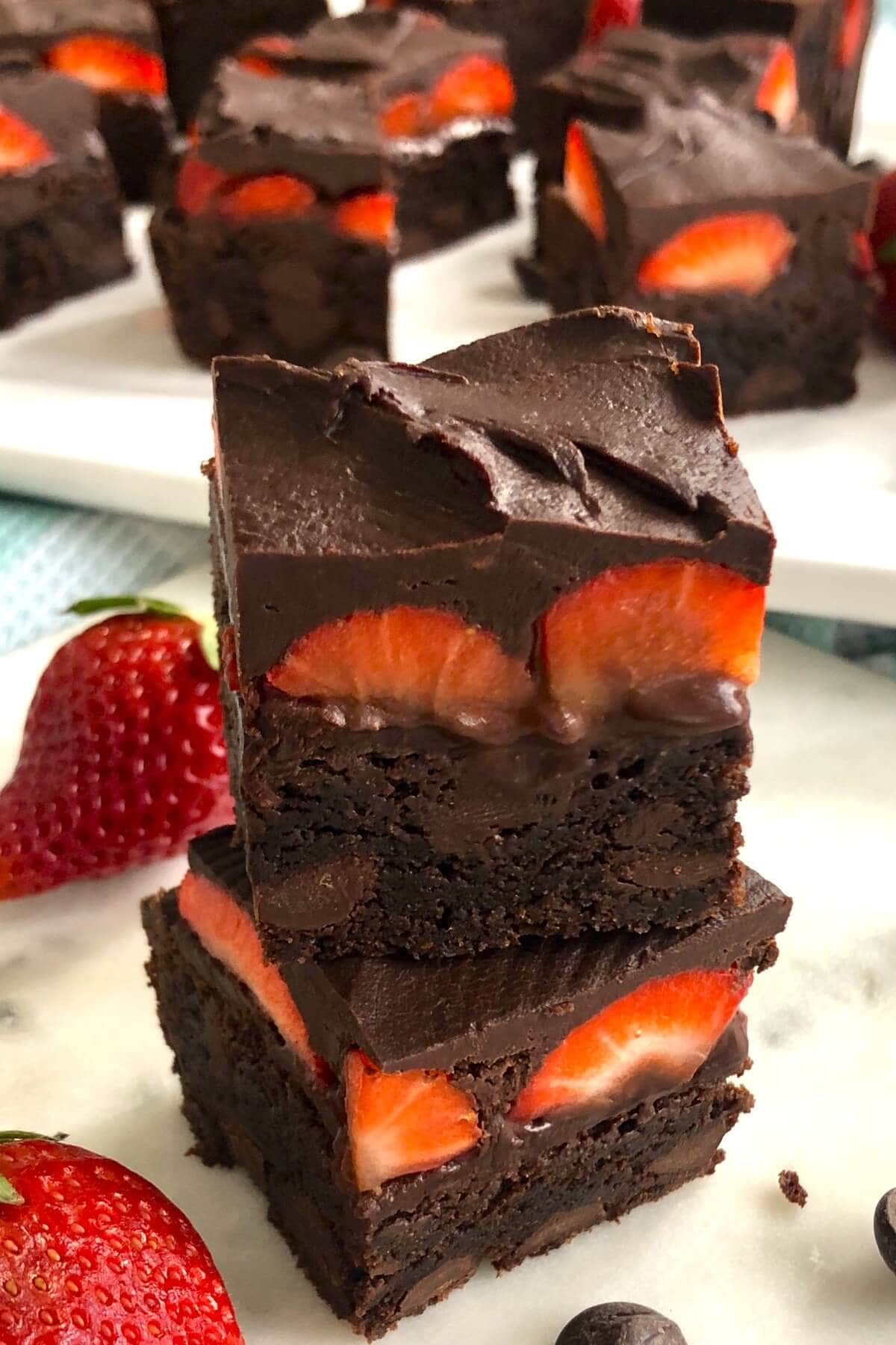 A stack of brownie with strawberries on a white marble board.