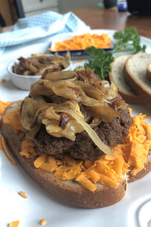 close up of sandwich with caramelized onions, cheddar cheese, and rye bread in background