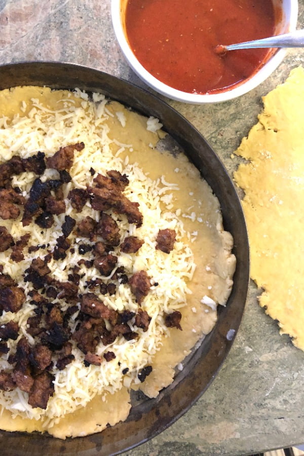 making a pizza with tomato sauce, Italian sausage and mozzarella cheese