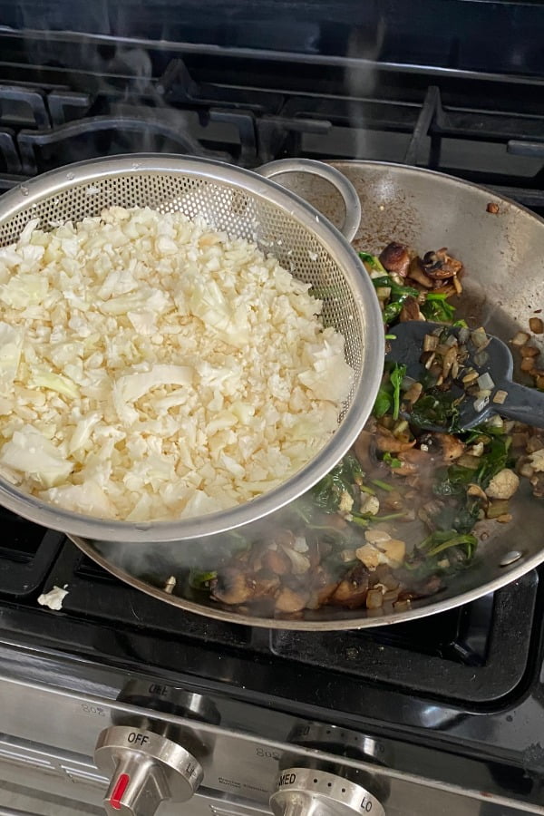 adding cauliflower rice to sauteed mushrooms, onions, and spinach