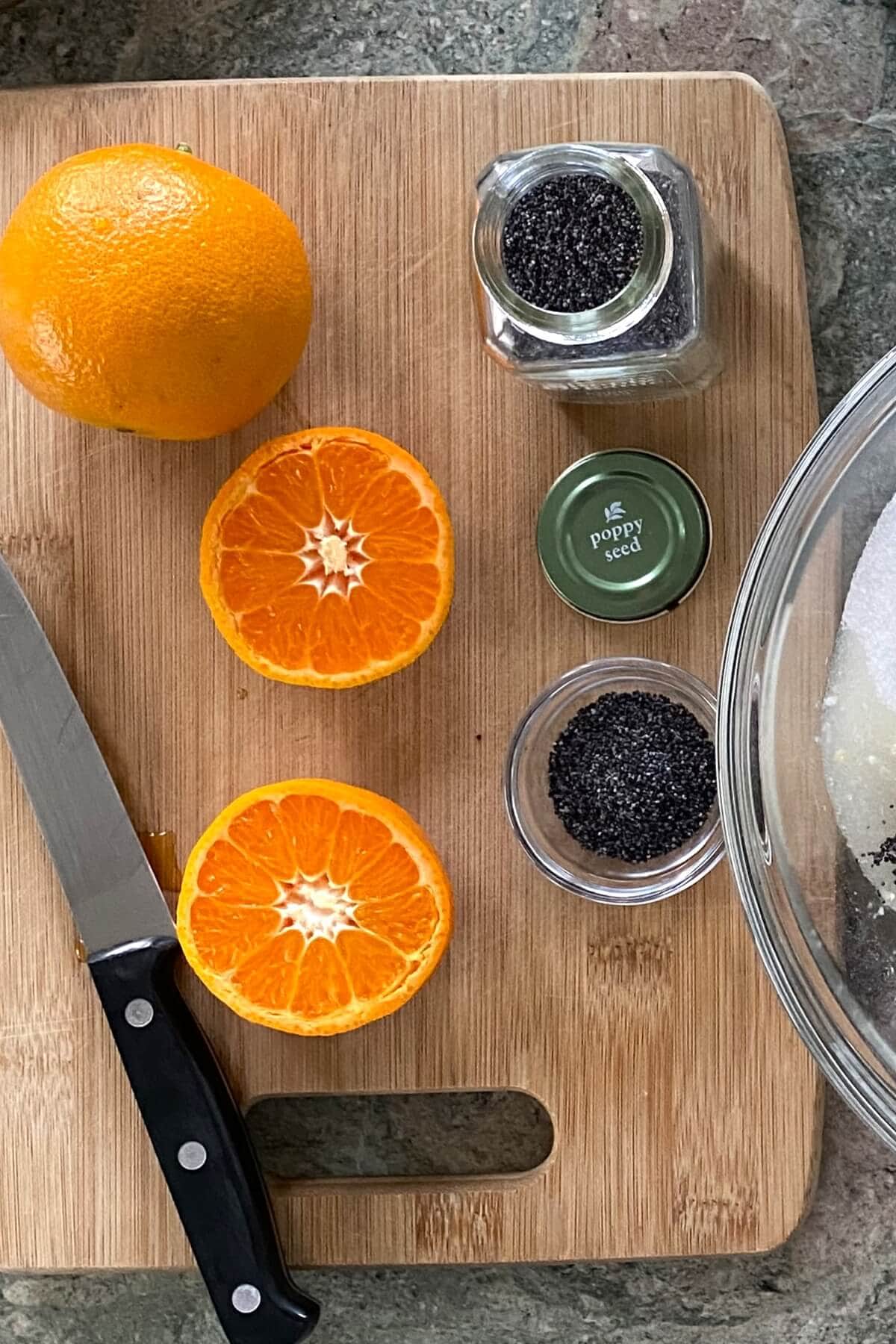 An orange and an orange cut in half and poppy seeds.
