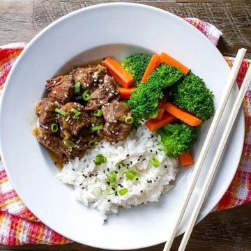 A bowl of Instant Pot Asian beef stew with rice, vegetables and chopsticks.