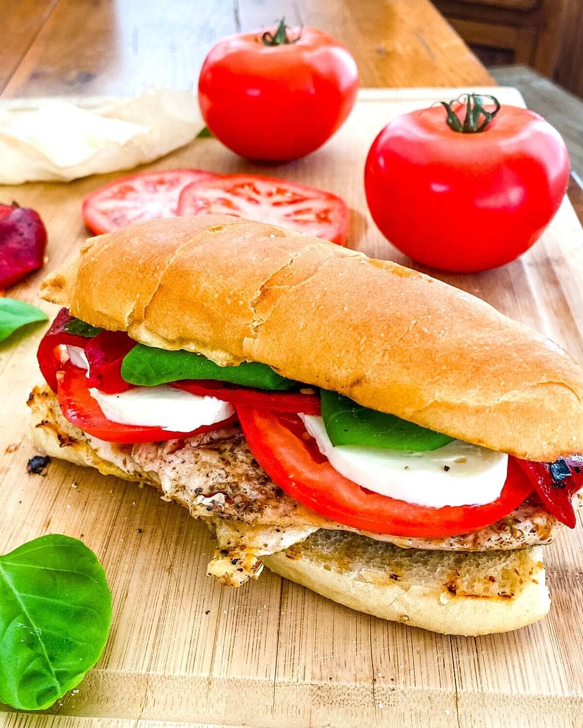 A whole chicken caprese sandwich in front of 2 tomatoes..