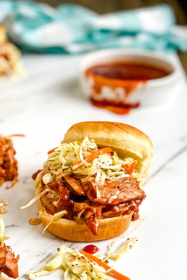 A mini bbq pork tenderloin slider with cole slaw and bbq sauce.