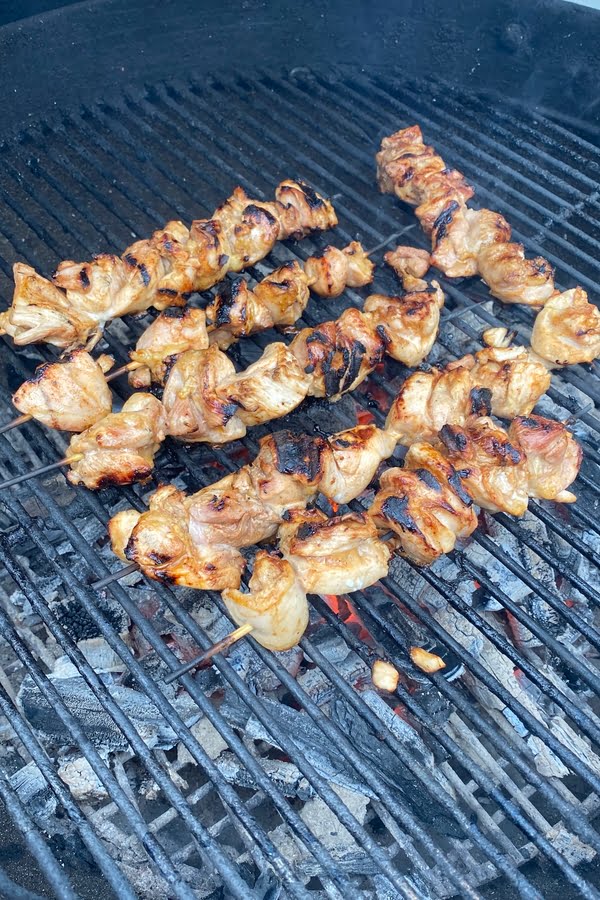 Grilling marinated chicken skewers on a charcoal grill.