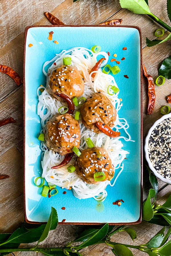 4 spicy General Tso's meatballs on a plate with rice noodles