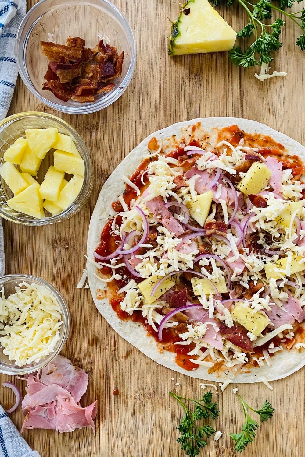 a tortilla pizza with ham, bacon and pineapple ready for the oven.