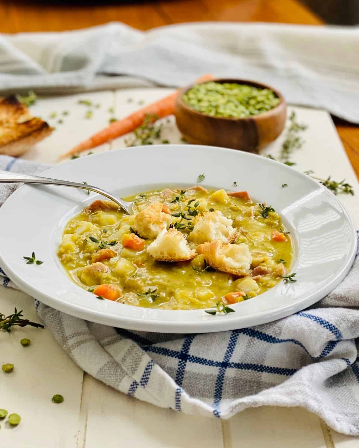 A bowl of split pea soup with ham and toasted croutons with a spoon in it.