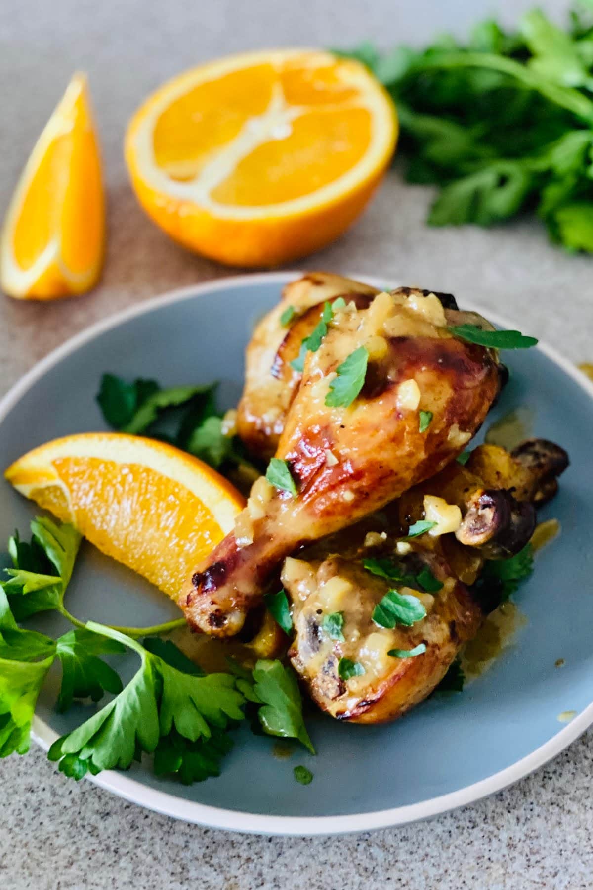3 oven roasted chicken legs on a plate with orange wedges