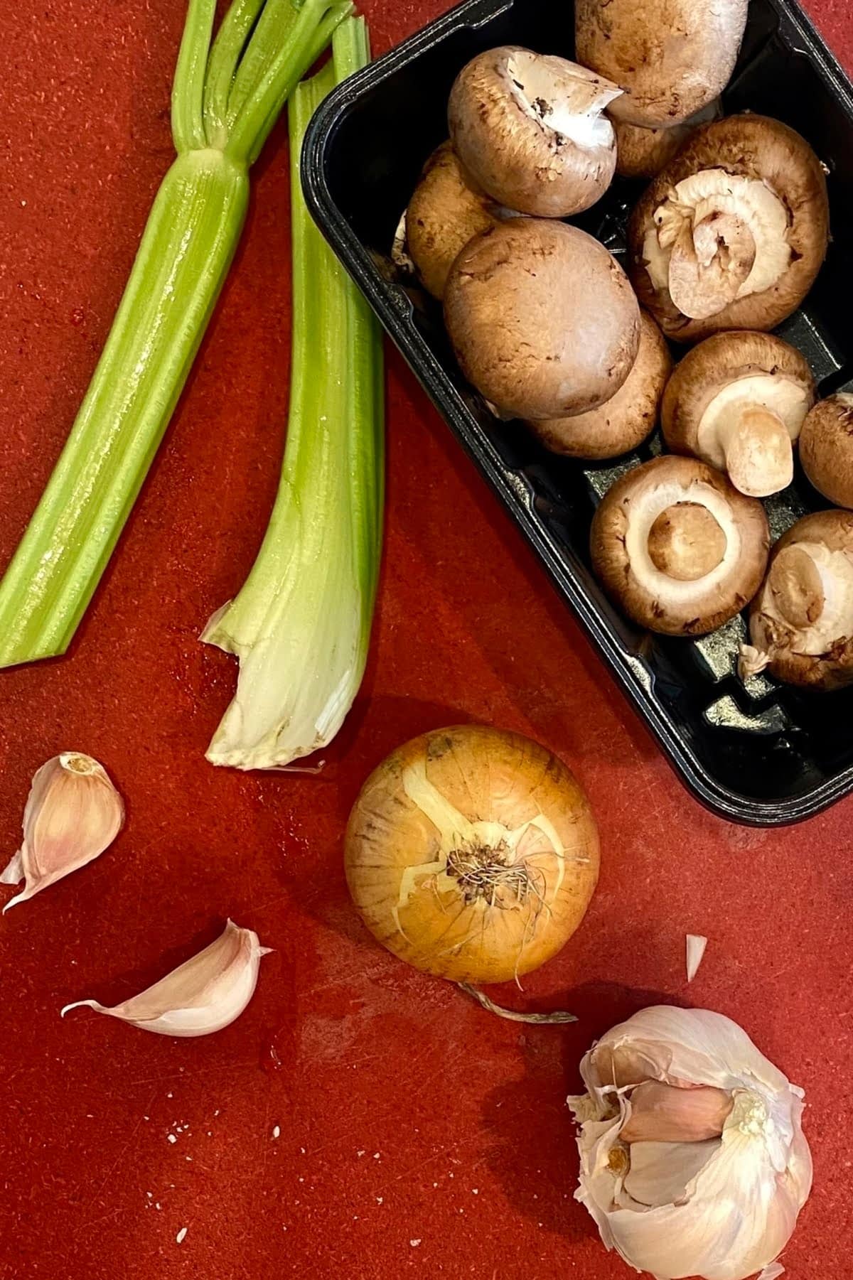Celery, garlic, onion, and mushrooms on a cutting board.