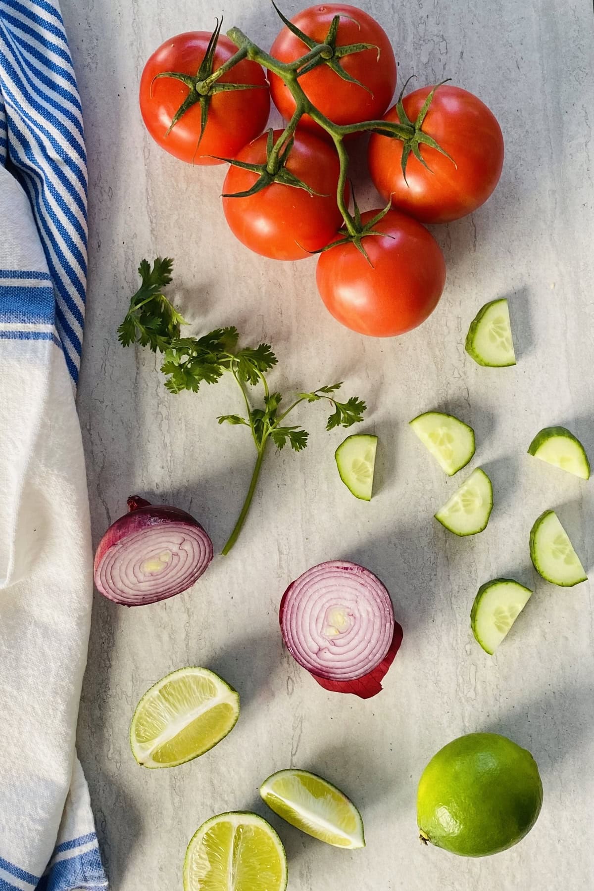 The ingredients for a Pico de Gallo recipe with fresh tomatoes, lime, red onion, cilantro, cucumber.