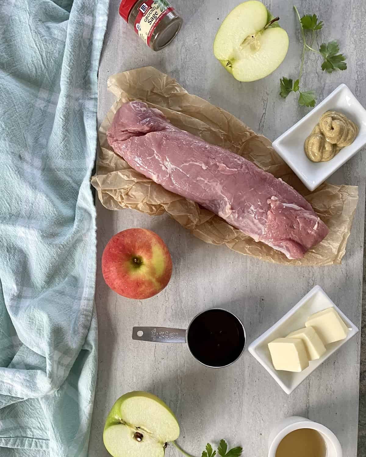 a pork tenderloin, apples, maple syrup, butter, mustard and ground sage on a marble counter.