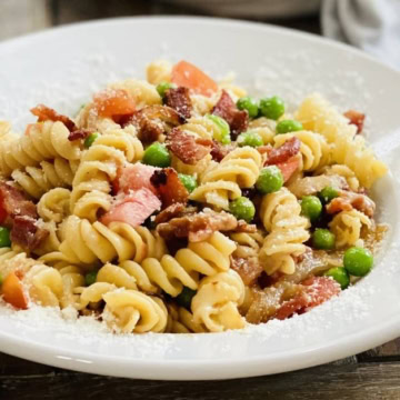 bowl of pasta with bacon, tomatoes, onions and peas.