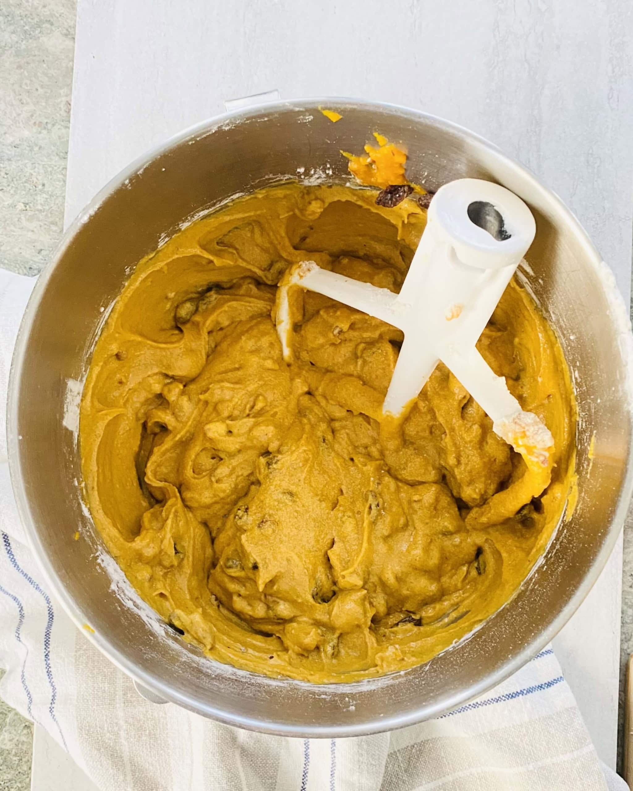 A mixing bowl with batter for pumpkin spice cookies with raisins and pecans.