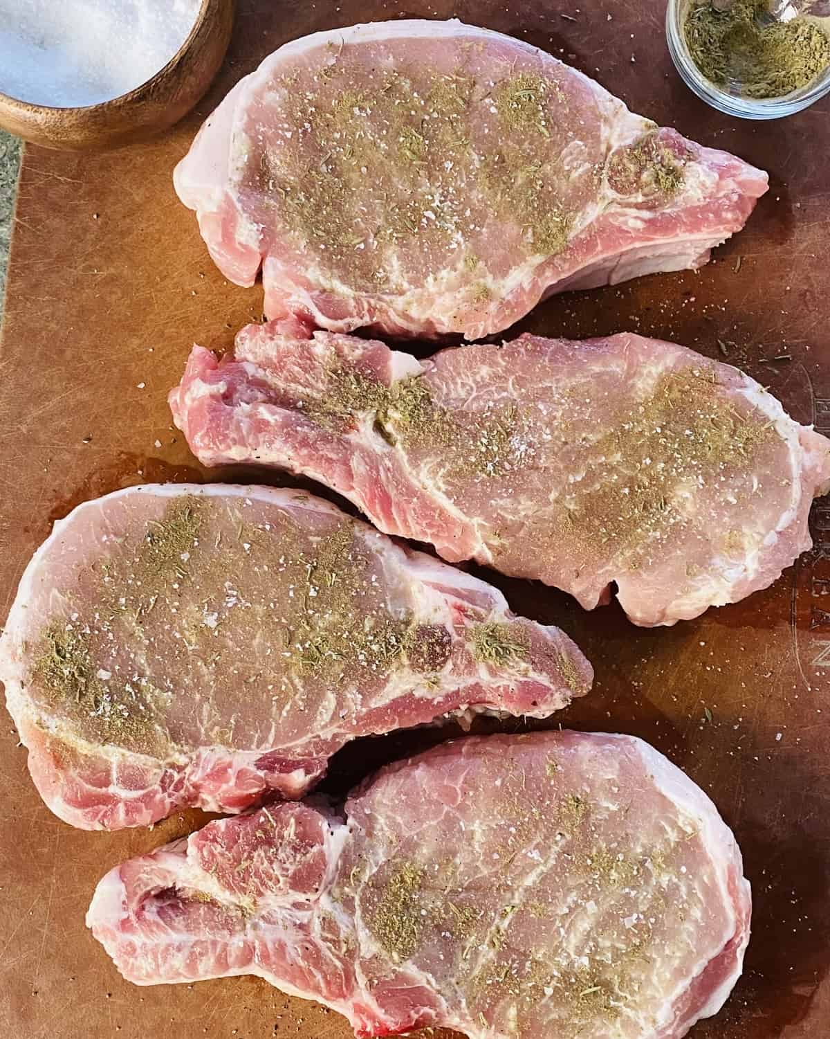 Seasoned pork chops on a cutting board.
