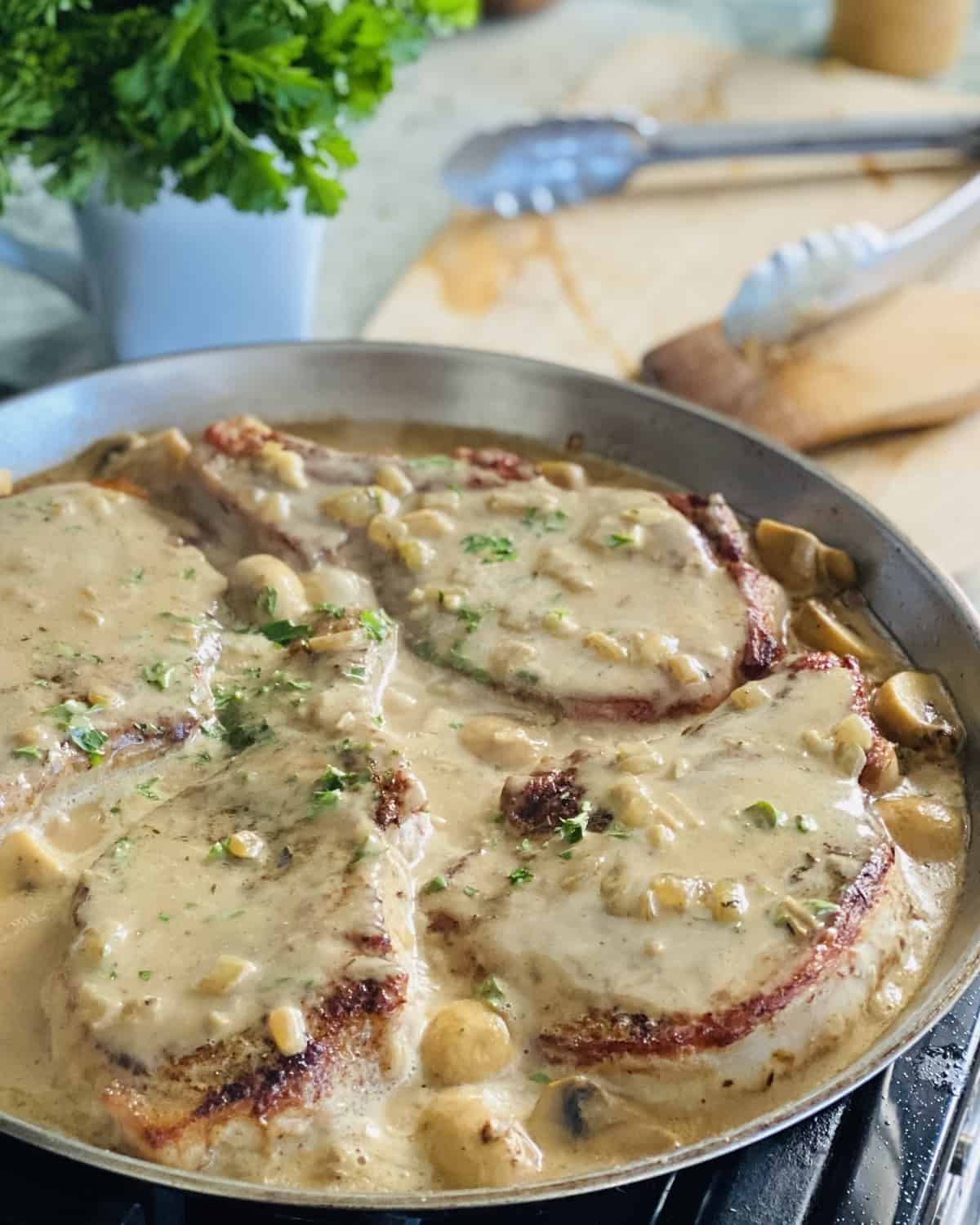 4 bone in pork chops in gravy in a pan.