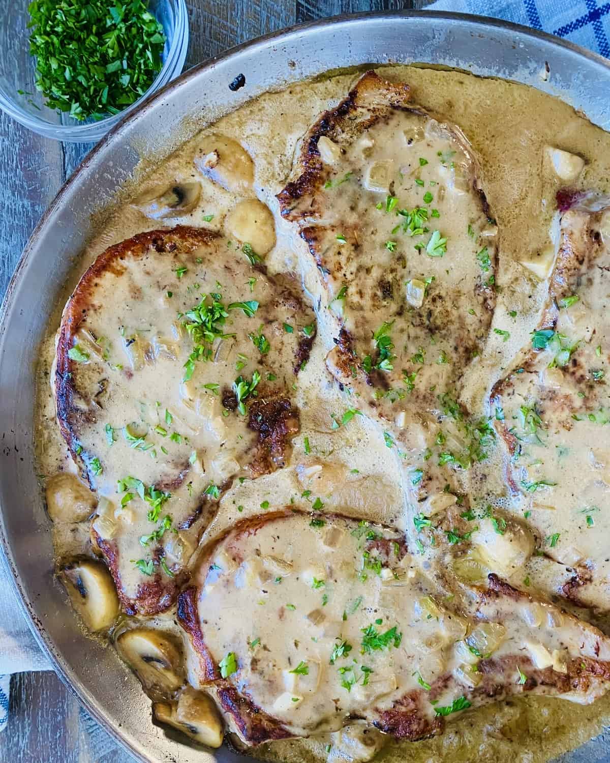 3 bone-in pork chops in mushroom gravy in a sauté pan.