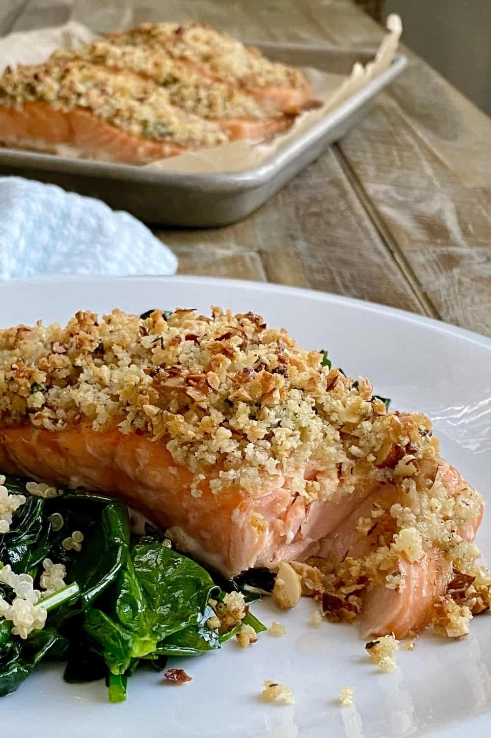 A piece of pecan crusted salmon on a plate with sauteed spinach and quinoa.