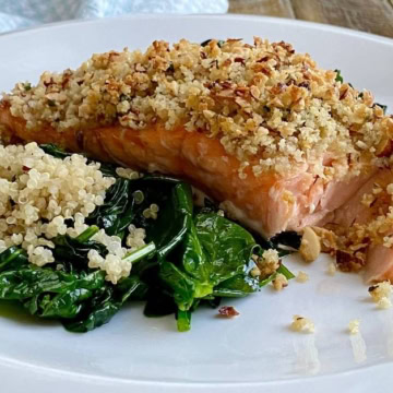 fillet of pecan crusted salmon on a plate with sauteed spinach and quinoa