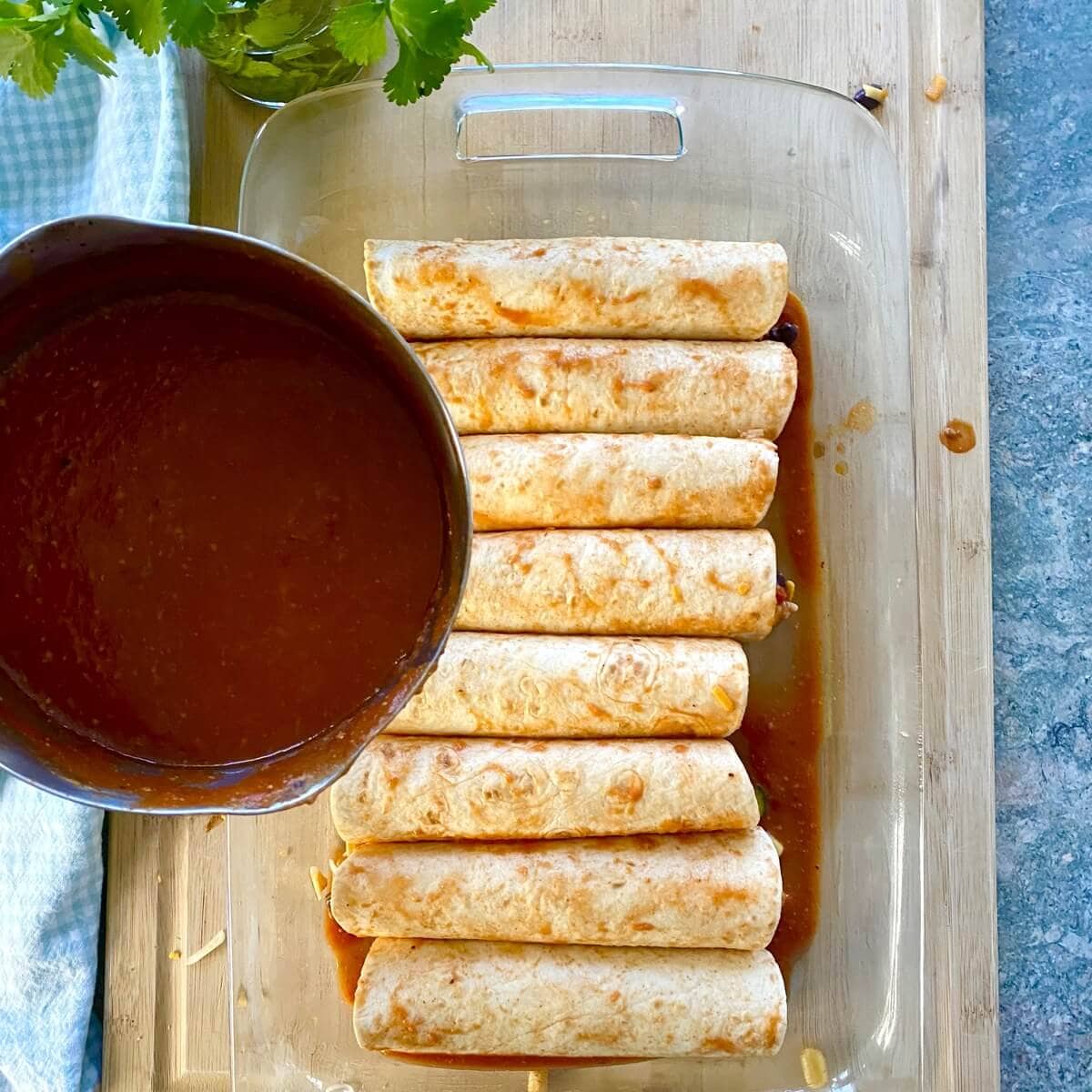 Topping unbaked enchiladas with red enchilada sauce.