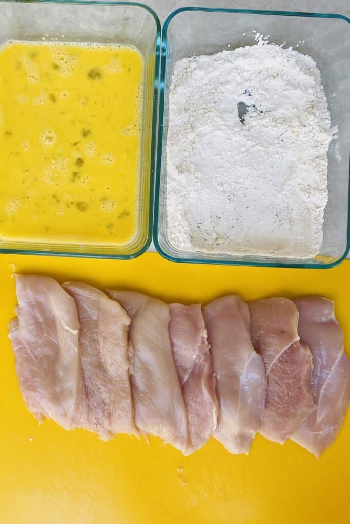 Chicken cutlets with beaten eggs, and flour on a counter.