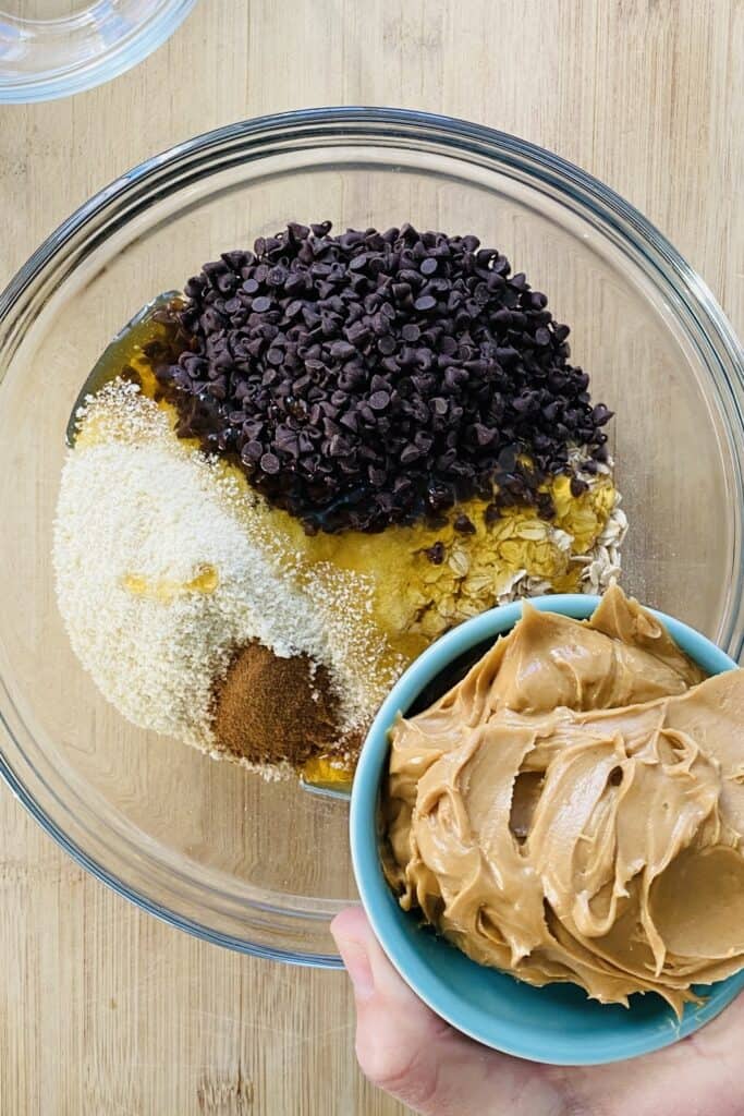 adding peanut butter to bowl with oats, honey, mini chocolate chips