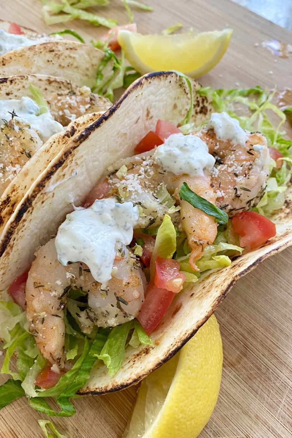 A shrimp taco with tzatziki sauce, chopped tomatoes and shredded lettuce.