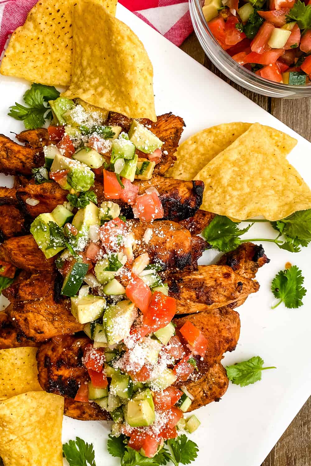 Chili rubbed chicken on a platter with avocado salsa and tortilla chips.