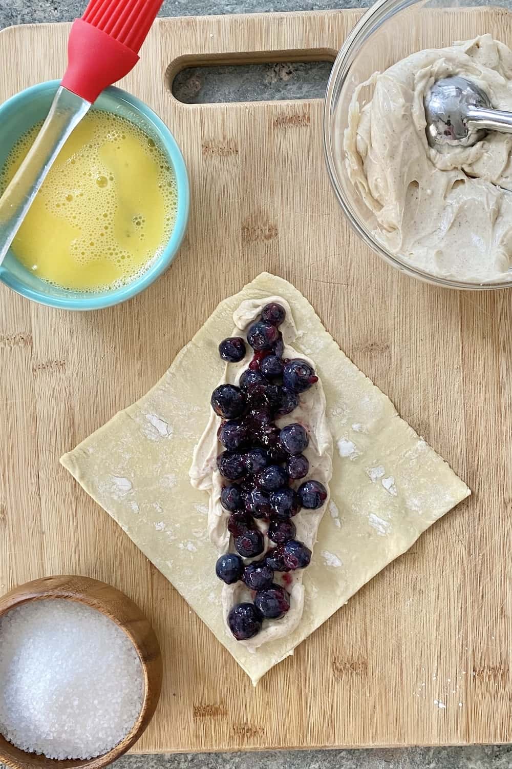 A puff pastry square topped with cream cheese filling and blueberries.
