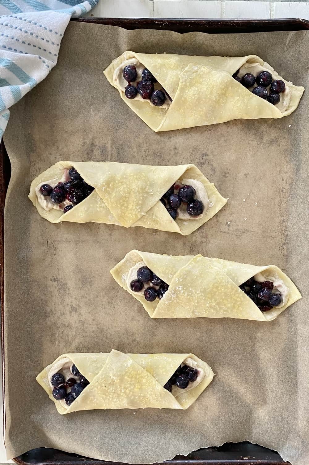 Unbaked blueberry and cheese danish on a baking sheet line with parchment paper.