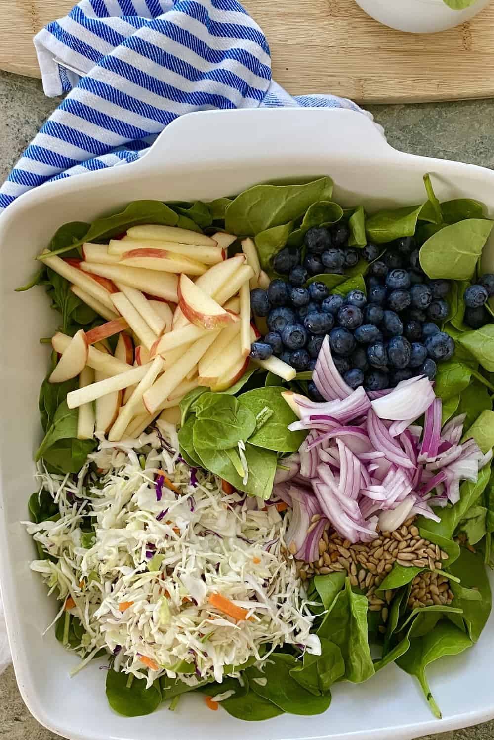 A spinach salad with apples, red onion, sunflower seeds.