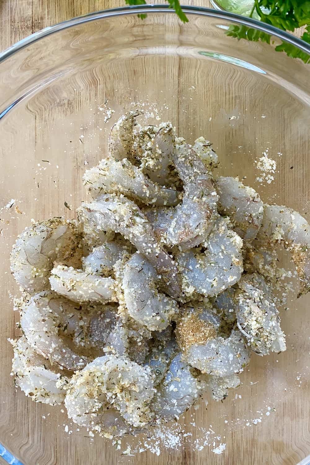 Shrimp tossed with seasonings in a glass bowl.