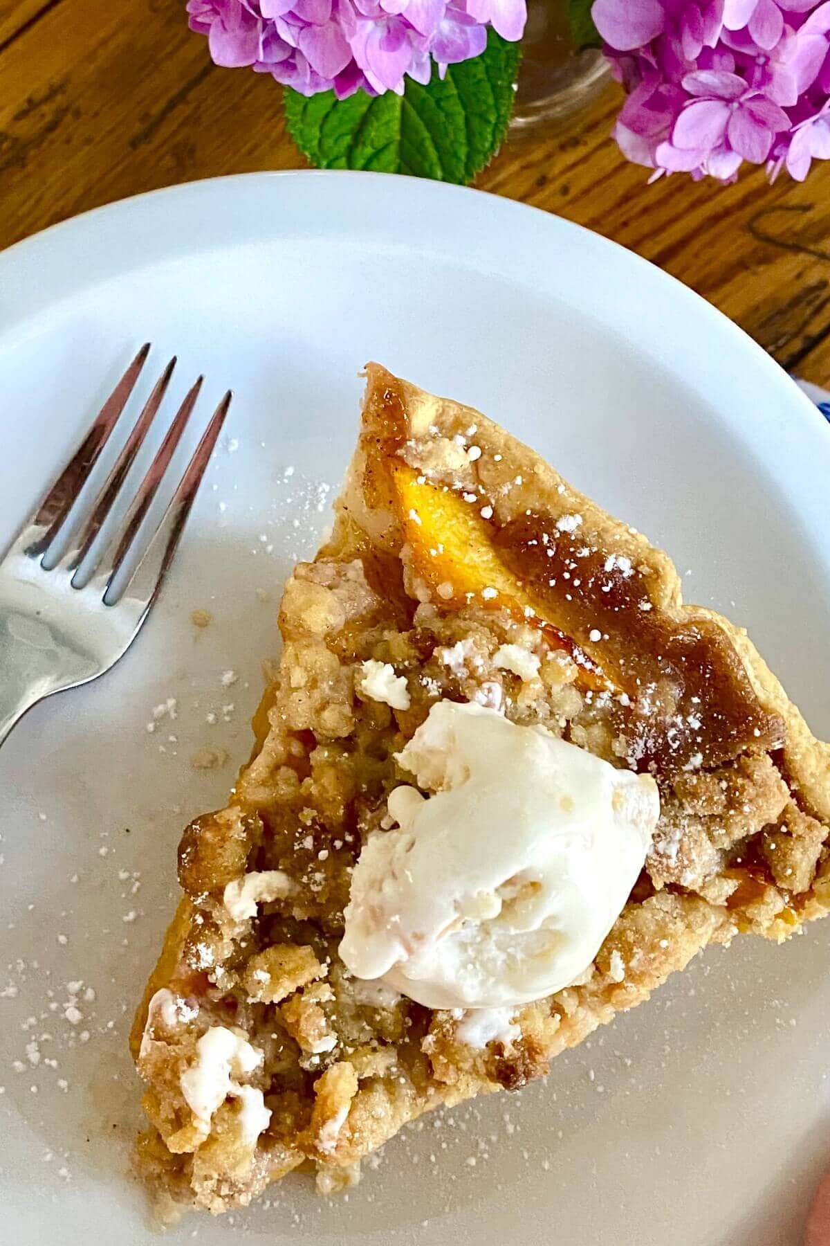A slice of peach crumble pie on a white plate.