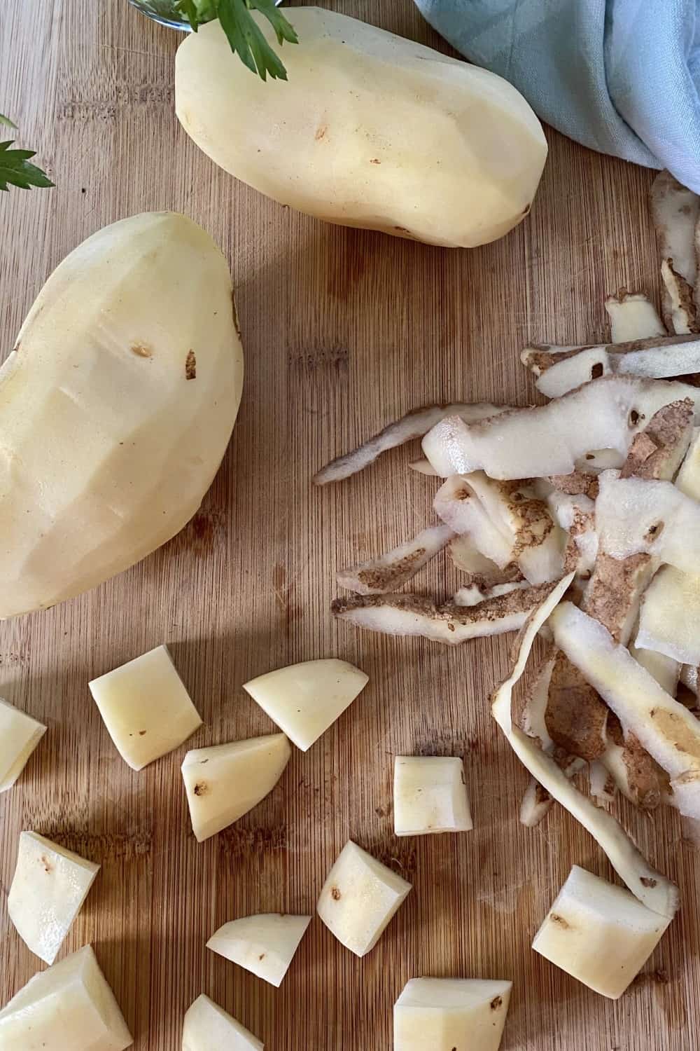 Peeled potatoes, cubed potatoes and potato peels on a cutting board.