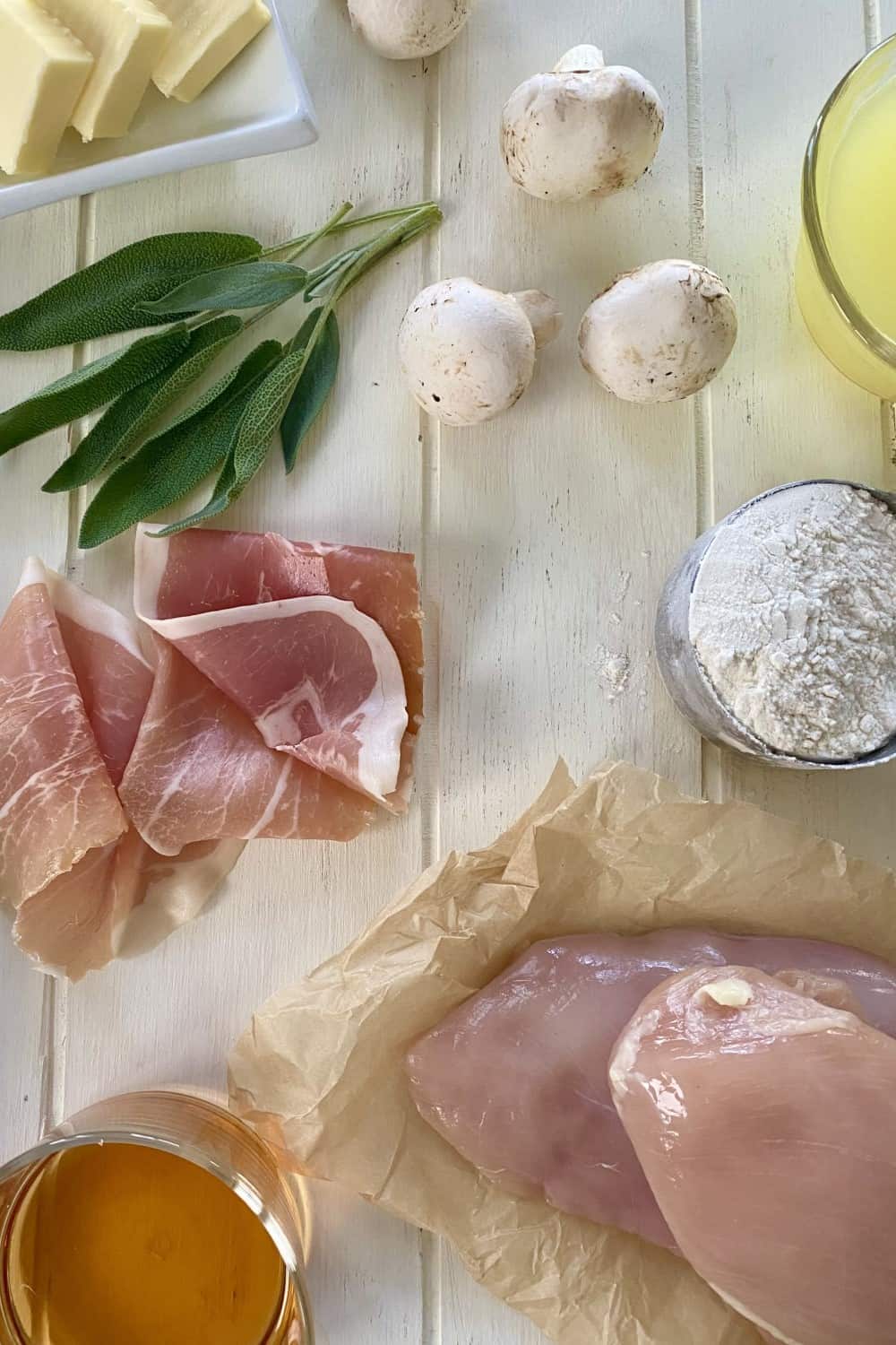 Mushrooms, prosciutto, chicken, sage, marsala, flour, and chicken stock on a wood counter.