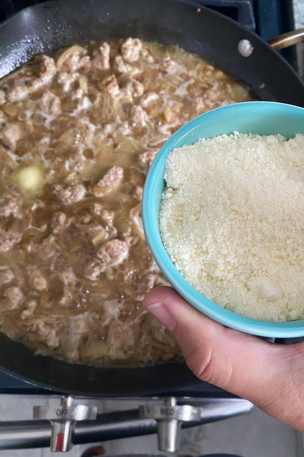 Adding grated parmesan cheese to a sausage sauce in a pan.